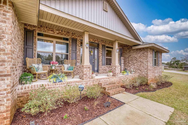 doorway to property with covered porch, brick siding, and board and batten siding