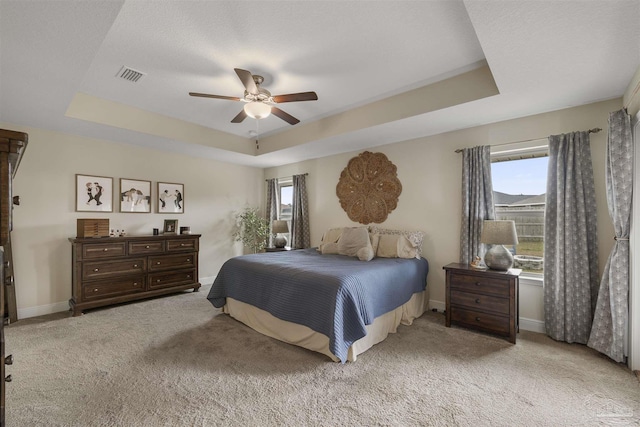 bedroom featuring light carpet, a tray ceiling, visible vents, and baseboards