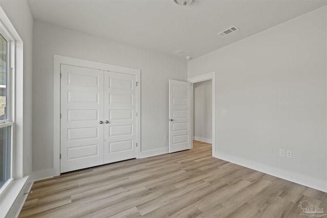 unfurnished bedroom featuring baseboards, light wood-style flooring, visible vents, and a closet