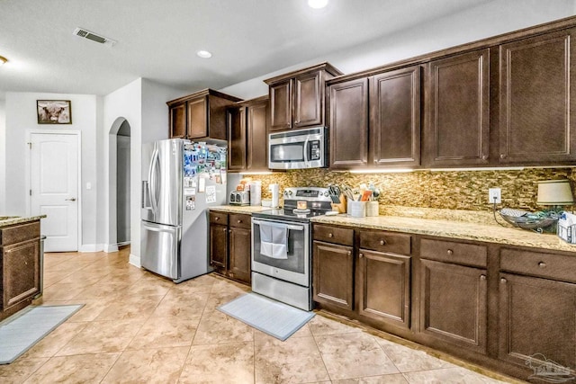 2704 Wildhurst Trl, Pace, FL 32571 - kitchen with stainless steel appliances, arched walkways, backsplash, dark brown cabinetry, and light stone countertops