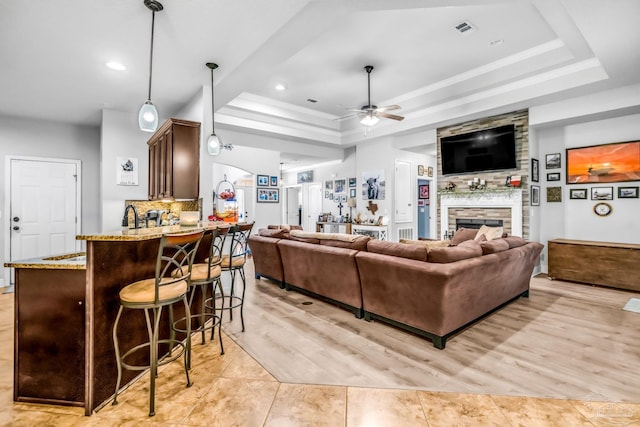 2704 Wildhurst Trl, Pace, FL 32571 - living room featuring a ceiling fan, a fireplace, a tray ceiling, recessed lighting, and light wood-type flooring