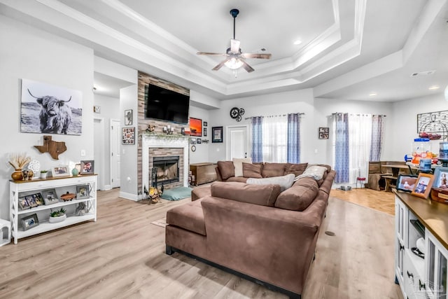 2704 Wildhurst Trl, Pace, FL 32571 - living room featuring ceiling fan, a stone fireplace, a raised ceiling, light wood-style flooring, and ornamental molding