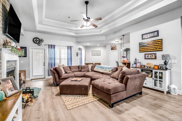 2704 Wildhurst Trl, Pace, FL 32571 - living area with a tray ceiling, light wood-style floors, a tiled fireplace, a ceiling fan, and ornamental molding
