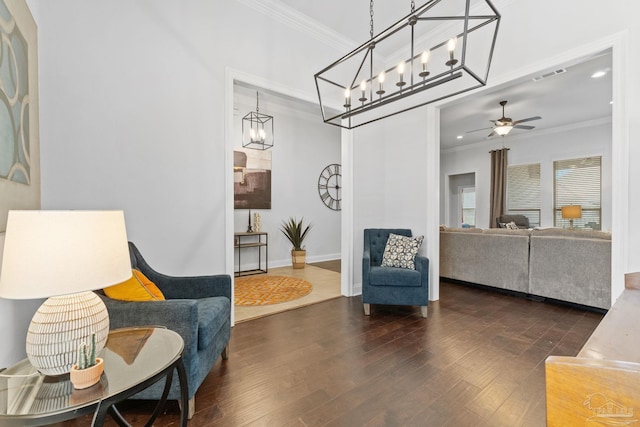 living area with visible vents, baseboards, dark wood-style flooring, ornamental molding, and ceiling fan with notable chandelier