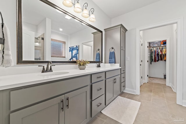 bathroom featuring a sink, double vanity, baseboards, tile patterned floors, and a walk in closet