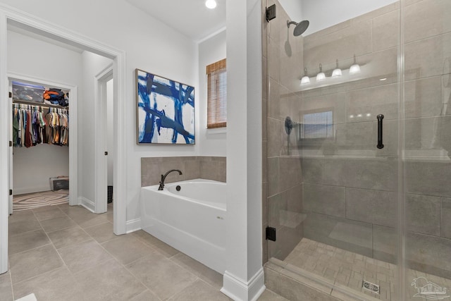 full bathroom featuring a shower stall, a bath, tile patterned floors, a walk in closet, and baseboards