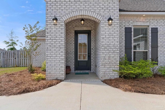 entrance to property featuring brick siding, fence, and a shingled roof