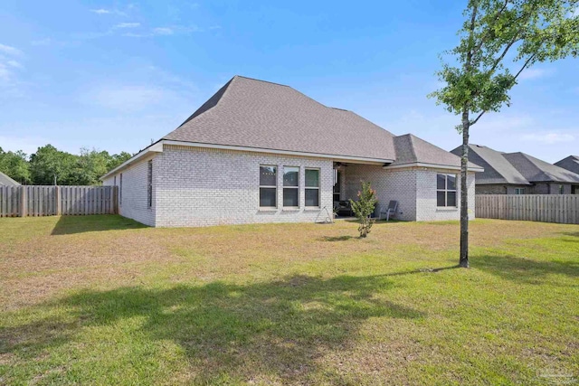 back of property with a lawn, a shingled roof, brick siding, and a fenced backyard