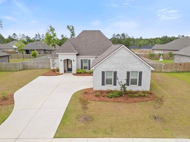 french provincial home with brick siding, fence private yard, a front yard, and concrete driveway