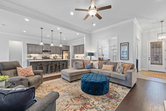 living room featuring dark wood finished floors, recessed lighting, ornamental molding, ceiling fan with notable chandelier, and baseboards