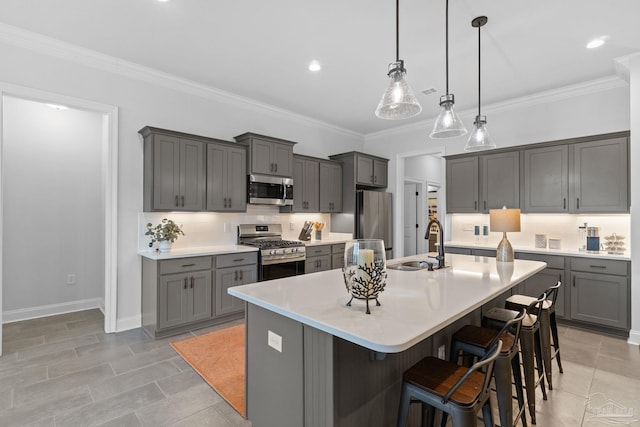 kitchen featuring a kitchen island with sink, a sink, a breakfast bar, gray cabinetry, and appliances with stainless steel finishes