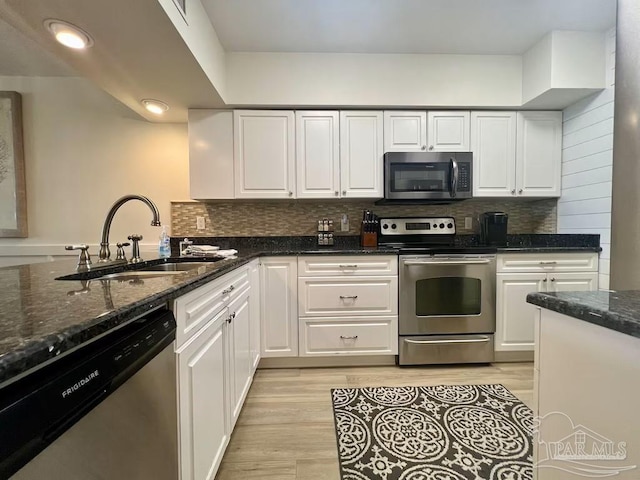 kitchen featuring white cabinetry, sink, dark stone counters, stainless steel appliances, and light hardwood / wood-style flooring