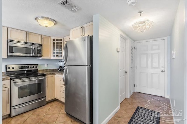 kitchen with light brown cabinetry, appliances with stainless steel finishes, a chandelier, and light tile patterned floors