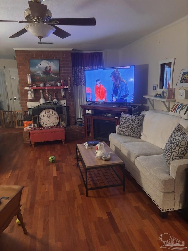 living room featuring ceiling fan, ornamental molding, hardwood / wood-style floors, and a brick fireplace