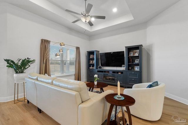 living room featuring ceiling fan, a tray ceiling, and light hardwood / wood-style floors