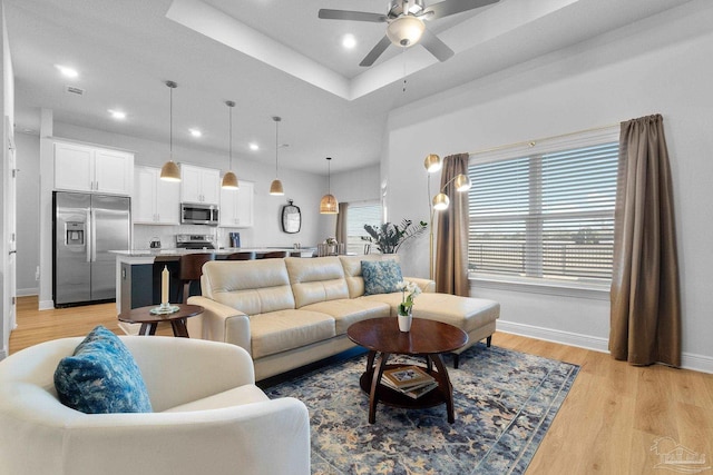 living room with ceiling fan, light hardwood / wood-style flooring, and a raised ceiling