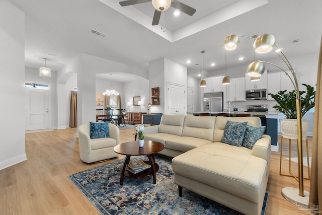 living room with ceiling fan with notable chandelier, sink, and light hardwood / wood-style flooring