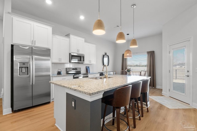 kitchen featuring decorative light fixtures, a center island with sink, sink, white cabinetry, and appliances with stainless steel finishes