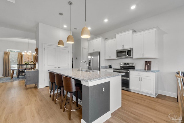 kitchen featuring white cabinetry, a center island with sink, stainless steel appliances, decorative light fixtures, and sink