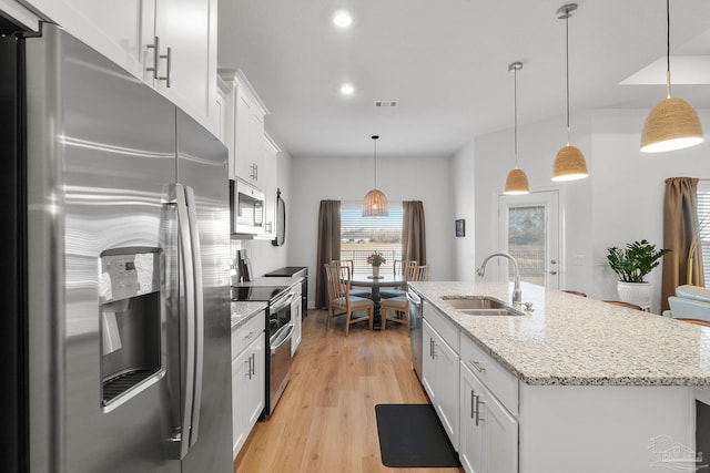 kitchen with appliances with stainless steel finishes, decorative light fixtures, white cabinetry, an island with sink, and sink