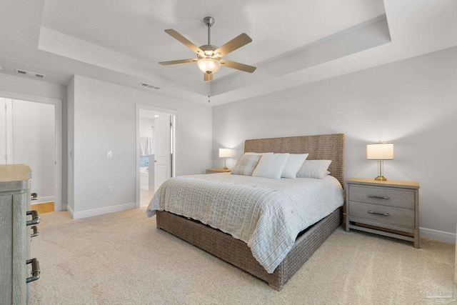 bedroom with light carpet, ceiling fan, a tray ceiling, and ensuite bath