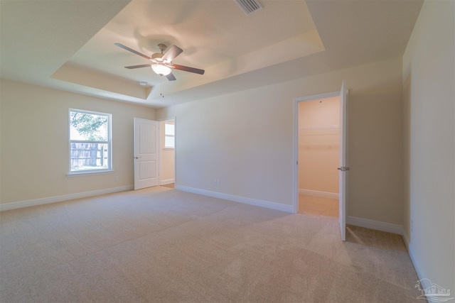 unfurnished room with light carpet, ceiling fan, and a tray ceiling