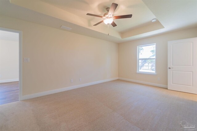 spare room with a raised ceiling, light colored carpet, and ceiling fan