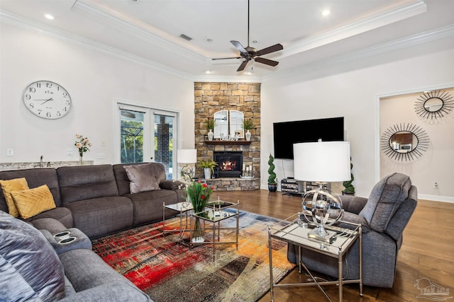 living room featuring a raised ceiling, a stone fireplace, ornamental molding, and hardwood / wood-style flooring