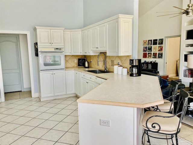 1358 Windsor Park Rd, Gulf Breeze, FL 32563 - kitchen featuring white oven, a peninsula, high vaulted ceiling, backsplash, and a kitchen bar