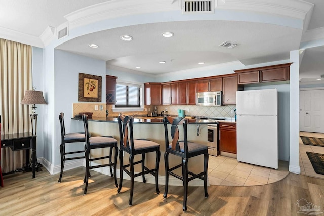 kitchen featuring kitchen peninsula, stainless steel appliances, ornamental molding, a kitchen bar, and light hardwood / wood-style floors