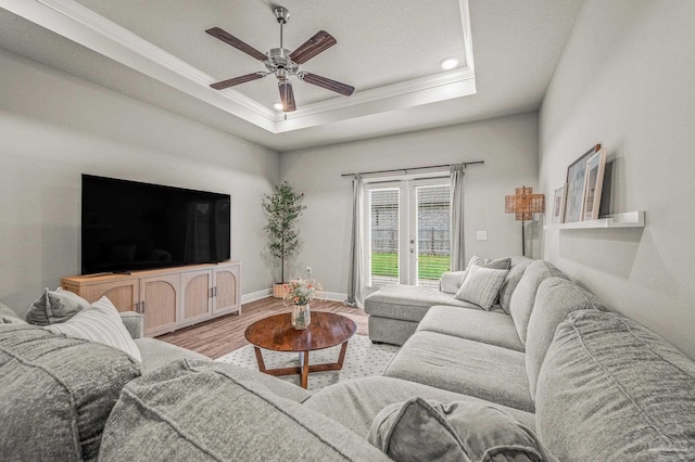 living area featuring ornamental molding, light wood finished floors, a ceiling fan, a tray ceiling, and baseboards