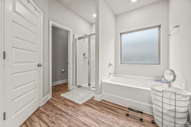bathroom with a stall shower, a garden tub, wood finished floors, baseboards, and recessed lighting