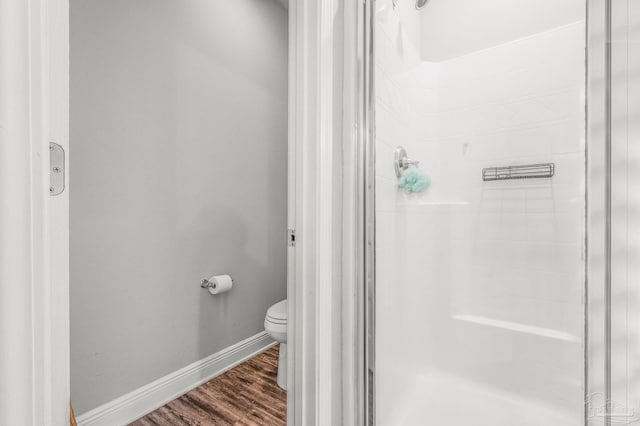 bathroom with a shower stall, toilet, wood finished floors, and baseboards