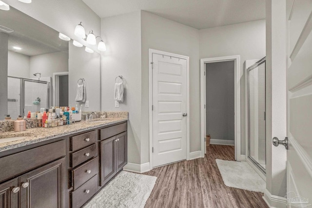 bathroom featuring a shower stall, wood finished floors, double vanity, and baseboards