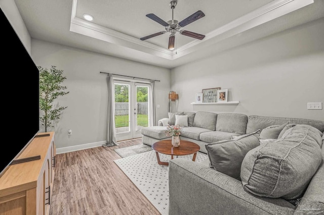 living room featuring ornamental molding, a tray ceiling, light wood-type flooring, a ceiling fan, and baseboards