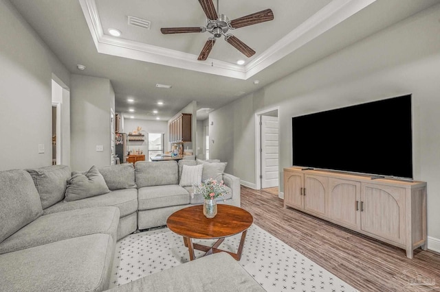 living area with crown molding, ceiling fan, recessed lighting, light wood-style flooring, and a raised ceiling