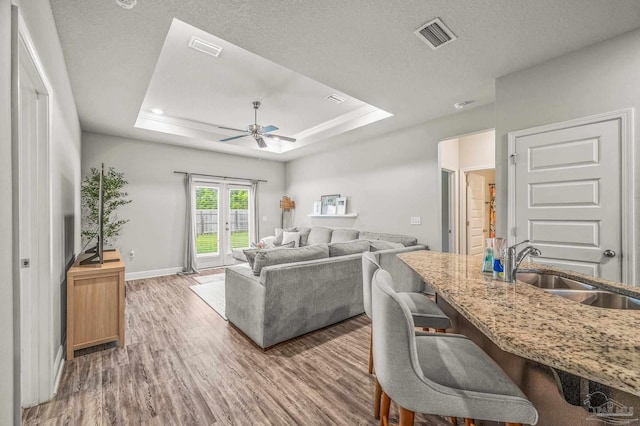 living room featuring ceiling fan, wood finished floors, a tray ceiling, baseboards, and a textured ceiling
