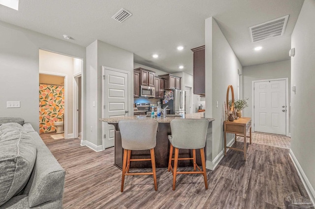 kitchen with stainless steel appliances, dark wood-style flooring, dark brown cabinetry, a kitchen breakfast bar, and baseboards