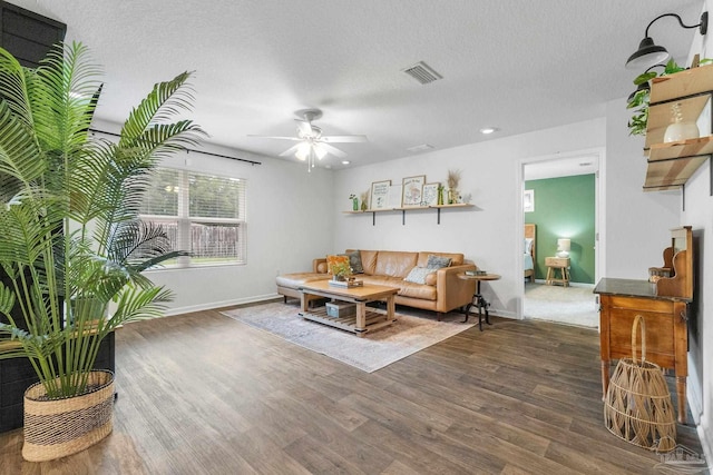 living room with a textured ceiling, ceiling fan, and dark wood-type flooring