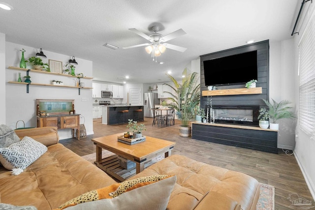 living room with ceiling fan, a large fireplace, wood-type flooring, and a textured ceiling