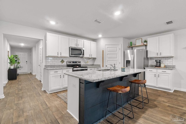 kitchen featuring white cabinetry, hardwood / wood-style floors, an island with sink, and appliances with stainless steel finishes