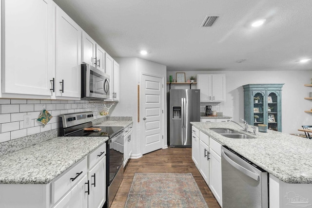 kitchen with appliances with stainless steel finishes, dark hardwood / wood-style flooring, a kitchen island with sink, sink, and white cabinets