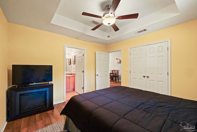 bedroom featuring hardwood / wood-style floors, a raised ceiling, ensuite bathroom, and ceiling fan