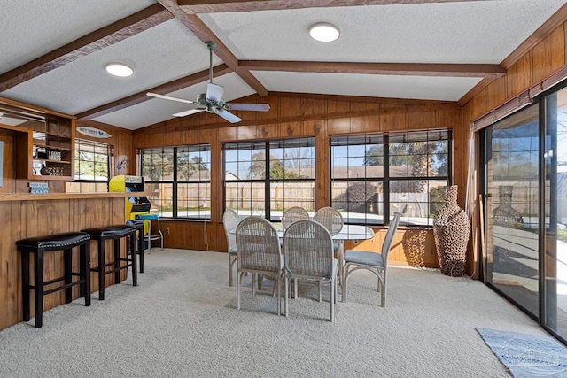 carpeted dining space featuring vaulted ceiling with beams, wooden walls, a textured ceiling, and ceiling fan