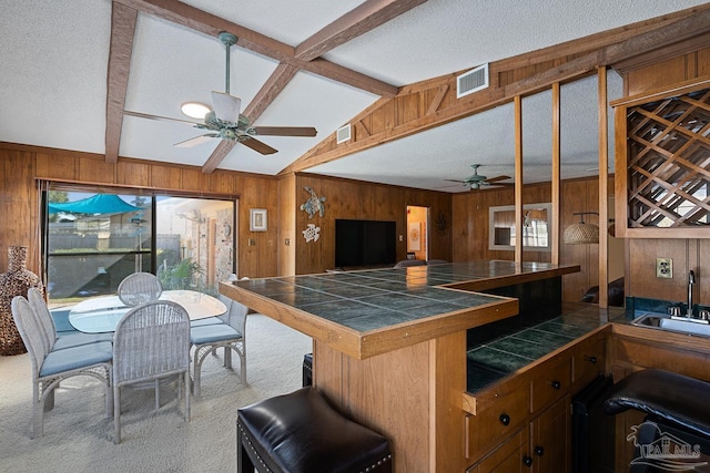 kitchen featuring sink, carpet flooring, tile counters, wooden walls, and ceiling fan