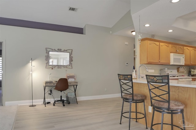 kitchen with a breakfast bar, light hardwood / wood-style floors, white appliances, and kitchen peninsula