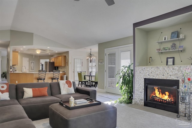 carpeted living room featuring sink, ceiling fan with notable chandelier, lofted ceiling, and a tiled fireplace