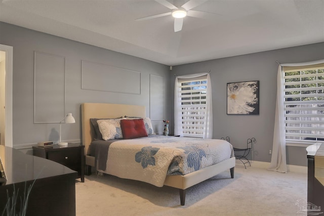 carpeted bedroom with a raised ceiling and ceiling fan