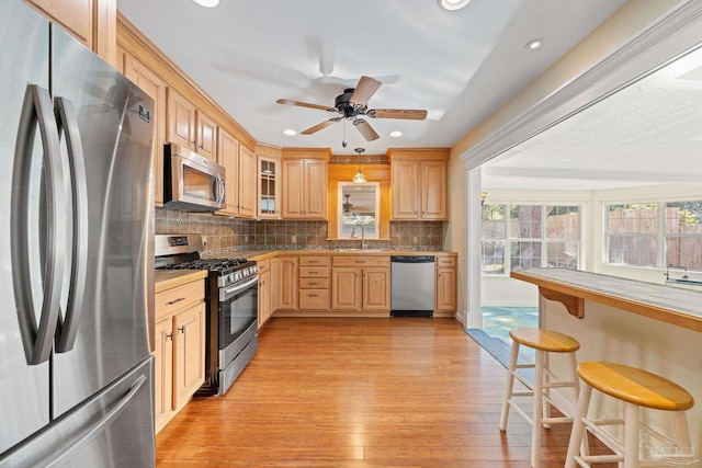 kitchen with light brown cabinetry, hanging light fixtures, sink, decorative backsplash, and stainless steel appliances