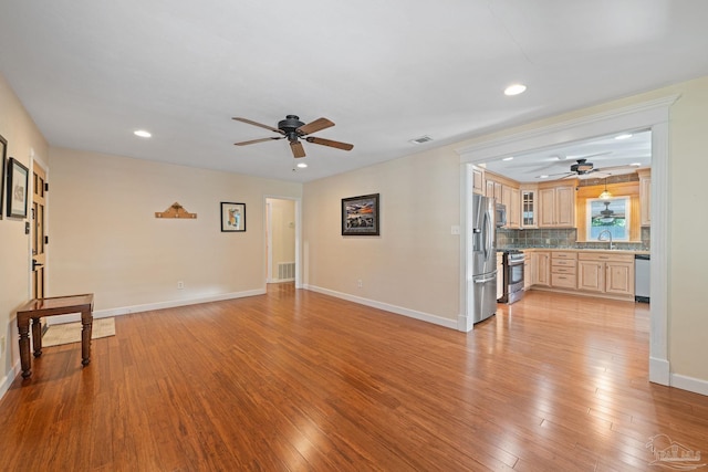 unfurnished living room featuring light hardwood / wood-style floors, sink, and ceiling fan